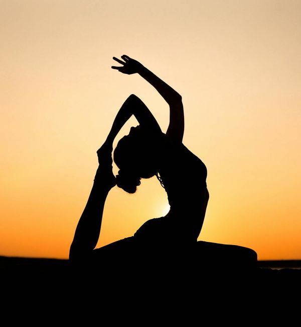 Silhouette of a person in a yoga balance pose against a sunset.